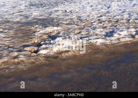 Schmutziger schmelzender Schnee mit nassem Sand im Spätwinter oder frühen Frühling. Wechselndes Wetter, Reinigung von Straßen, Parks und Straßen im Frühjahr. Kommunale Dienstleistungen Stockfoto