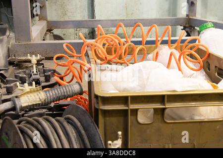 Der Kompressor und der Schlauch sowie der Draht auf der Rolle und den Kästen in der Nähe befinden sich auf dem Boden in der Lackiererei, die Arbeitsausrüstung befindet sich in der Werkstatt Stockfoto