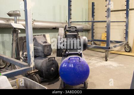 Der Kompressor befindet sich auf dem Boden in der Malerwerkstatt, die Arbeitsausrüstung befindet sich in der Werkstatt Stockfoto