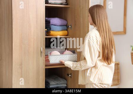 Eine junge Frau, die saubere Kleidung in den Kleiderschrank faltet Stockfoto