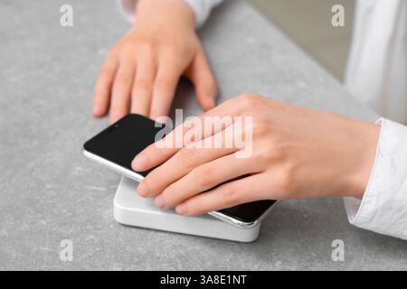 Frau, die modernes Handy auf das drahtlose Ladegerät auf dem Tisch legt, Nahaufnahme Stockfoto