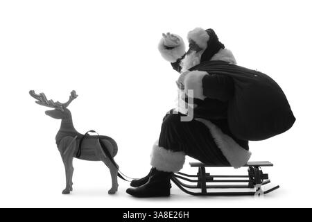 Silhouette des Weihnachtsmanns mit Geschenktüte auf Schlitten und Rentier aus Holz vor weißem Hintergrund Stockfoto