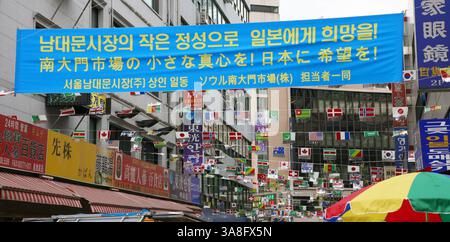 SEOUL, SÜDKOREA. APRIL 2011. Ein Banner, das Hoffnung für Japan wünscht, hängt über der Namdaemun Market Street mit Weltflaggen in Seoul. Stockfoto