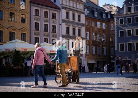 Warschau. März 2025. Ein Busker begrüßt ein Paar, das am 28. März 2025 in der Altstadt von Warschau vorbeiläuft. Quelle: Jaap Arriens/Xinhua/Alamy Live News Stockfoto