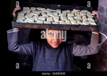 Peking, Ägypten. März 2025. Ein Kind trägt am 27. März 2025 ein Tablett mit traditionellen Keksen auf dem Kopf vor Eid al-Fitr in Kairo, Ägypten. Quelle: Ahmed Gomaa/Xinhua/Alamy Live News Stockfoto