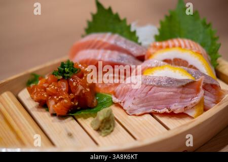 Sashimi-Set mit Lachs, serviert auf einem hölzernen Sushi-Boot, mit Zitrone und Wasabi Stockfoto