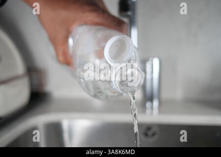 Gießen Sie klares Wasser aus einer Plastikflasche in ein Spülbecken Stockfoto