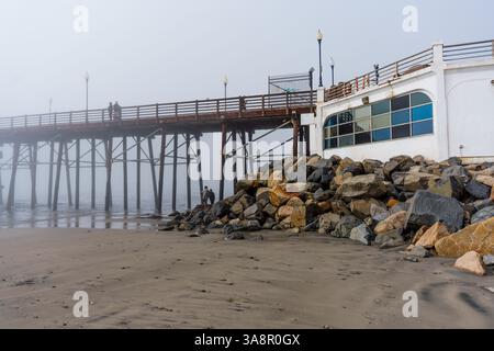 Oceanside, Kalifornien - 3. Januar 2025: Ruhiger, nebeliger Morgenblick auf den Oceanside Municipal Pier mit felsigen Küsten und dem berühmten Gebäude, Stockfoto