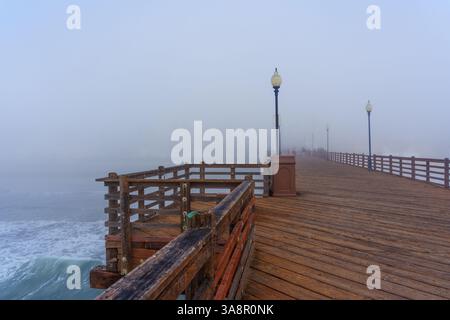 Oceanside, Kalifornien - 3. Januar 2025: Weitwinkelansicht des Oceanside Municipal Pier, umgeben von dickem Nebel, mit Holzgeländern und Lamppo Stockfoto