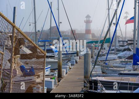 Oceanside, Kalifornien - 3. Januar 2025: Ruhige nebelige Morgenszene am Oceanside Harbor mit Booten und einem Leuchtturm inmitten von Masten und einem ruhigen geldautomaten Stockfoto