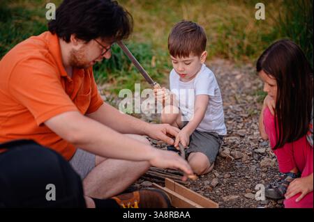 Ein Vater und seine Kinder nehmen an einer Outdoor-Aktivität Teil und lernen gemeinsam Überlebensfähigkeiten. Die Einstellung schlägt Camping, Pfadfinder oder Bushc vor Stockfoto