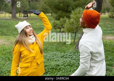 Junge Männer und Frauen in Winterkleidung, die im Park High 5 geben und gemeinsam einen Wintertag genießen Stockfoto