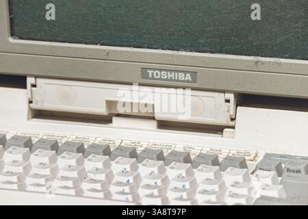 Triest, Italien - 18. August 2024: Ein alter Toshiba-Laptop, mit staubiger Tastatur und leerem Bildschirm, in einem Vintage-Ambiente. Stockfoto
