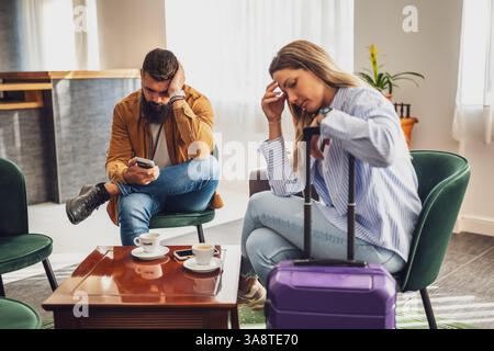 Mann und Frau sitzen in der Lobby am Flughafen und warten auf das Boarding. Sie sind gelangweilt und müde. Stockfoto