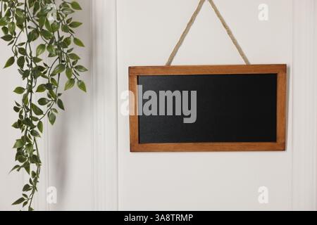 Leere kleine Tafel und grüne Zimmerpflanze an weißer Wand Stockfoto