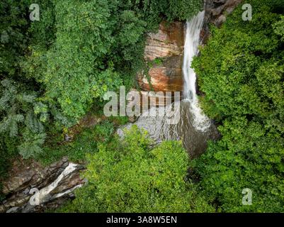 Das Bild zeigt den geheimen Wasserfall in Illukpelessa, Sri Lanka, umgeben von dichtem tropischem Grün. Das Wasser kaskadiert über zerklüftete Felsen in eine Tra Stockfoto