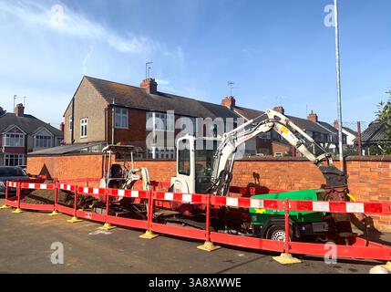 Straßenbauarbeiten in Northampton England Großbritannien Gasundichtigkeit Grabbagger Wandhaus Häuser Schilder Poller Poller lokaler Platz geparkt Mini Cabrio Loch in Stockfoto