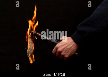Molotow Cocktail wird mit einem Feuerzeug auf dunklem Hintergrund, Nahaufnahme, selektiver Fokus entzündet. Konzept: Straßenunruhen, revolutionäre Bewegung, Verteidigung und Stockfoto