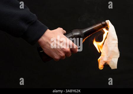 Molotow Cocktail wird mit einem Feuerzeug auf dunklem Hintergrund, Nahaufnahme, selektiver Fokus entzündet. Konzept: Straßenunruhen, revolutionäre Bewegung, Verteidigung und Stockfoto