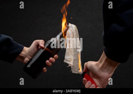 Molotow Cocktail wird mit einem Feuerzeug auf dunklem Hintergrund, Nahaufnahme, selektiver Fokus entzündet. Konzept: Straßenunruhen, revolutionäre Bewegung, Verteidigung und Stockfoto