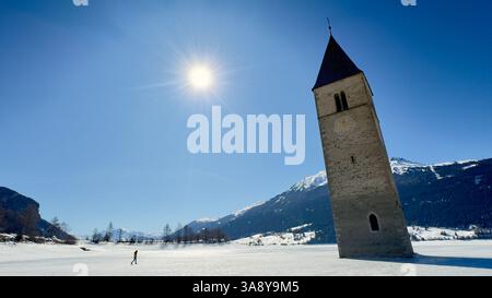 Der sonnendurchflutete Kirchturm des Reschensees entspringt aus dem gefrorenen Reschensee in Südtirol Stockfoto