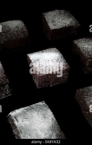 Eine Nahaufnahme eines quadratischen Stücks Brownie mit Puderzucker darüber. Der Kuchen ist von anderen quadratischen Kuchenstücken umgeben Stockfoto