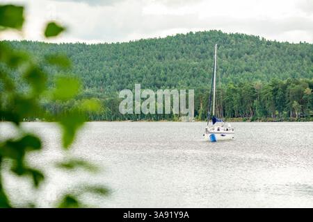 Der Turgojak-See im südlichen Ural in Russland. Ein weißes Segelboot schwimmt im Wasser. Das Boot ist mit Lichtern dekoriert. Es gibt mehrere Leute Stockfoto