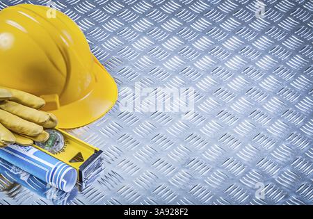 Zusammensetzung der blau gerollten Blaupausen des Bauhelms Sicherheitshandschuhe Konstruktionsebene auf gerilltem Metallhintergrund Stockfoto