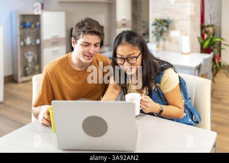 Ein multiethnisches Paar, das einen Laptop nutzt und zu Hause Kaffee trinkt, genießt einen entspannenden Moment zusammen Stockfoto