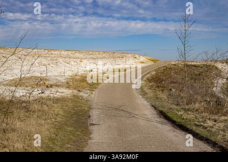 Malerischer Blick auf eine gewundene asphaltierte Straße inmitten von Küstendünen, die zu einem klaren blauen Himmel führt Stockfoto