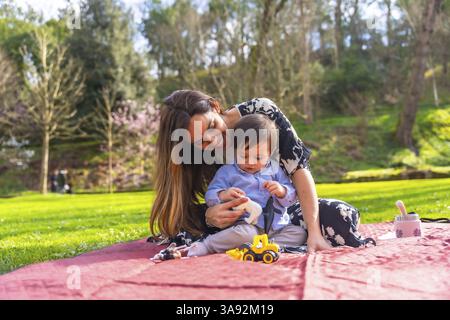 Mutter und Sohn genießen eine gute gemeinsame Zeit und spielen im Frühling mit Spielzeug auf einer Decke in einem lebhaften Park Stockfoto