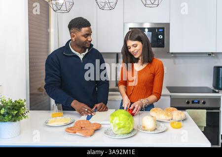 Junge multiethnische Paare bereiten Burger zum Abendessen zu und genießen ihre gemeinsame Zeit in einer modernen und hellen Küche Stockfoto