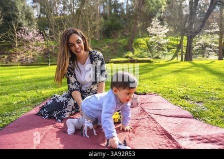 Mutter und Baby genießen eine gute gemeinsame Zeit, spielen mit Tierspielzeug auf einer Decke in einem sonnigen Park und schaffen eine herzerwärmende Szene der Familienbindung Stockfoto