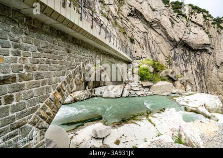 Ein Gebirgszug in den Schweizer Alpen, durch den ein Fluss fließt. Der Fluss ist von grünen Bäumen umgeben. Die Berge sind mit Schnee bedeckt. Teufel Stockfoto