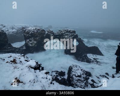 Schneebedeckte Gatklettur-Felsbogen in Arnarstapi, Island. Eine natürliche Basaltbrücke, die vom Meer geschnitzt wurde, mit Wellen, die in einer atemberaubenden Winte darunter krachen Stockfoto