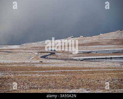 Einsames Haus und gewundene Straße in verschneite isländische Landschaft unter einem dunklen Winterhimmel. Abgelegene und friedliche Landschaft auf der Halbinsel Snæfellsnes Stockfoto