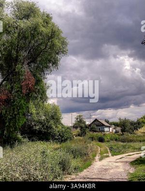 Ländliche Schotterstraße, die zu einem alten Holzhaus unter dramatischen Sturmwolken auf dem Land führt Stockfoto