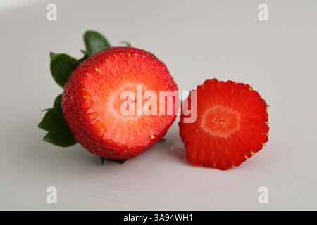Zwei Hälften einer frischen Erdbeere auf einer weißen Oberfläche. Nahaufnahme mit saftiger Textur, lebendigen Farben und natürlichen Details bei weichem Licht. Stockfoto