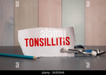 Arzt schreibt in Notizbuchwörtern TONSILLITIS auf weißem Hintergrund mit Stethoskop. Medizinisches Konzept Stockfoto