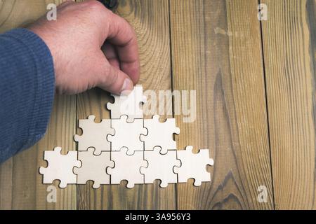 Menschliche Hand platziert ein Puzzleteil oben auf der Pyramide, die aus Puzzles gebildet wird. Das Konzept des Unternehmenserfolgs und des Unternehmergeistes. Stockfoto