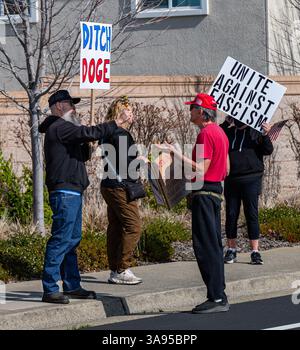 Ein Unterstützer von Trump und Musk verwickelt sich mit einem Mann, der bei einem Protest in einem Tesla-Händlerbetrieb Glocken schüttelt. Stockfoto