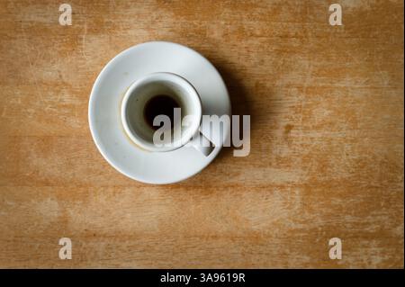 Weiße Keramik Espresso-Tasse und Untertasse mit Kaffeetassen auf einer alten braunen Holzplatte, von oben. Stockfoto