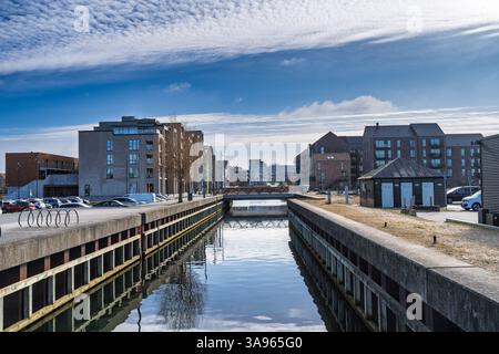 Ruhige urbane Kanalszene mit moderner Wohnarchitektur, lebhaften Reflexionen im Wasser und klarem blauem Himmel, die ein ruhiges Stadtleben umschließt Stockfoto