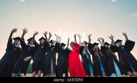Begeisterte Absolventen in akademischer Kleidung und Mortarboards feiern fröhlich ihre akademische Leistung im Freien Stockfoto