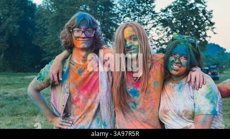 Schulfreunde feiern holi mit pulsierendem Puder und umarmen sich gegenseitig in bunten Festlichkeiten Stockfoto