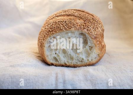 In Scheiben geschnittenes Sesambrot auf einem groben Hanftuch. Sauerteigbrot mit Sesamsamen bestreut. Kopierbereich. Stockfoto