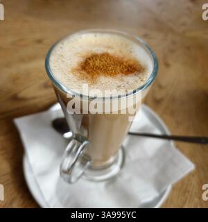 Ein schäumender, cremiger veganer Chai Latte Drink mit Hafermilch auf einem Holztisch mit langem Metalllöffel, in einem hohen Glas mit Serviette. Stockfoto
