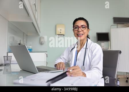 Glückliche reife ärztliche Fachärztin, die am Arbeitsplatz sitzt Stockfoto