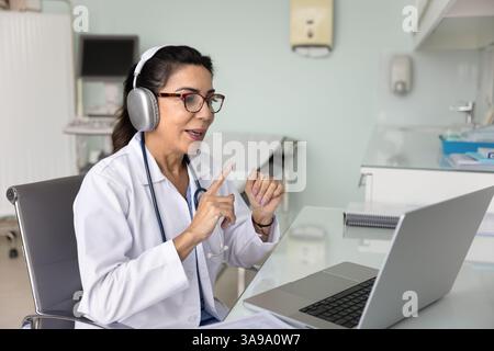 Ältere Reife Ärztin in Kopfhörern, die auf der Telehealth-Konferenz spricht Stockfoto