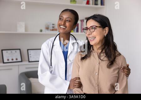 Glückliche junge schwarze Ärztin und ältere Frau, die wegblickt Stockfoto